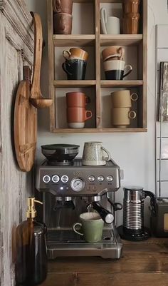 an espresso machine sitting on top of a wooden counter next to a shelf filled with cups