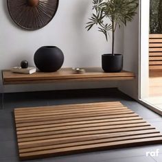 a wooden table with two black vases on it and a plant in the corner