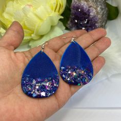 Fun and classy dangling teardrop earrings painted with the art of resin in dark blue and embellished with glass with hints of purple. They can easily transition from day to night. Made on a wood base that is light on your ears and won't pull. Specifications Proudly handmade Hand painted, resin, wood, glass Stainless steel French earwire Nickel free Silica earring backs Approximate measurements: 3in from top of earwire, 1.5in on widest part. Branded earring card and box included How to prolong th Blue Resin Teardrop Earrings, Blue Teardrop Pendant Earrings As Gift, Blue Teardrop Resin Jewelry, Unique Teardrop Resin Earrings, Handmade Teardrop Resin Earrings, Handmade Resin Teardrop Earrings, Unique Blue Teardrop Earrings For Gift, Resin Teardrop Earrings For Gifts, Handmade Teardrop Earrings For Party