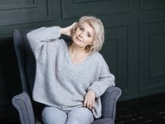 a woman sitting in a chair with her hand on her head and looking at the camera