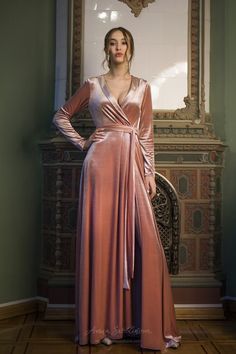 a woman standing in front of a mirror wearing a long pink dress with a wrap around the waist