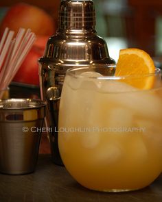 an orange slice in a glass next to a cocktail shaker