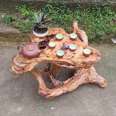 a table made out of tree branches with tea cups on it and plants in the background