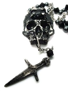 Made to Order! A universal memento mori for your dark wardrobe, this skull pendant is complete with a small dagger to enhance its grim aura. An imposing complement to your most dramatic looks, the pendant is cast in lead free pewter by hand and weathered, then set with a glass or stone cabochon. The chain is accented with hand beaded elements for a finishing touch. It can be layered with one of my rosary chains, or shorter pieces like chokers! Its also perfect on its own with all kinds of outfit choices as a centerpiece. Available in multiple variants Necklace chain default length: 18 in If you'd like a different chain length, please leave a note with your order Time to make and ship: 1-2 days. Black Skull Necklace In Edgy Style, Black Edgy Skull Necklace, Black Gothic Necklaces For Larp, Medieval Black Metal Necklace, Medieval Style Black Metal Necklace, Gothic Skull Jewelry With Skull Print, Gothic Metal Skull Necklace, Gothic Silver Necklace With Skull Print, Black Skull Necklace With Oxidized Finish