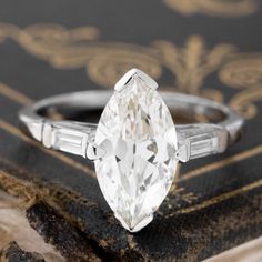 an old - fashioned diamond engagement ring sits on top of a piece of paper next to a book