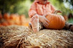 a small child sitting on top of hay next to a pumpkin