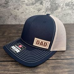 Celebrate the incredible bond between fathers and their children with our Richardson 112 Hat, featuring a genuine leather patch with a "Dad" subtitle. This hat makes for a meaningful Father's Day gift, especially for first-time dads or expecting fathers.Crafted with care, this hat showcases both style and comfort. The Richardson 112 design is renowned for its quality, featuring a structured, mid-profile fit and a pre-curved visor that adds a touch of classic appeal. The genuine leather patch, pr Outdoor Trucker Hat For Father's Day, Adjustable Flat Bill Snapback Hat For Father's Day, Father's Day Trucker Hat For Outdoor, Father's Day Outdoor Trucker Hat, Adjustable Trucker Hat With Curved Brim For Father's Day, Father's Day Trucker Baseball Cap With Curved Brim, Father's Day Trucker Hat In Baseball Cap Style, Adjustable Flat Bill Dad Hat For Father's Day, Father's Day Outdoor Trucker Hat With Curved Bill