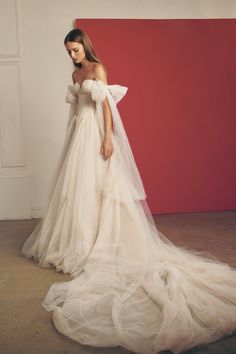 a woman in a white wedding dress standing next to a red wall