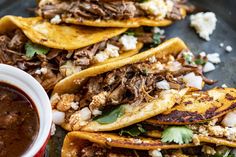 some tacos with meat, cheese and sauce on a black plate next to a cup