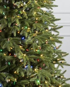 a small christmas tree with multicolored lights in front of a white wall and door