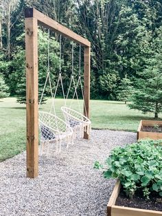 two white hammock chairs sitting on top of a gravel covered ground next to trees