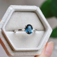 a ring with a blue topaz sits in a white velvet box on a table