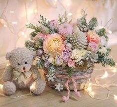 a teddy bear is sitting next to a basket with flowers and pine cones in it