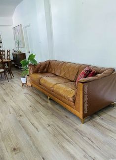 a brown leather couch sitting on top of a wooden floor next to a dining room table