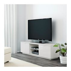 a flat screen tv sitting on top of a white entertainment center next to a potted plant