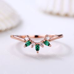 a rose gold ring with green and white stones on the side, sitting on top of a