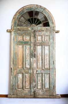 an old wooden door with arched glass on the top and bottom panel, in front of a white wall