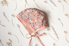 a pink hat with flowers on it sitting on top of a white table next to dried plants