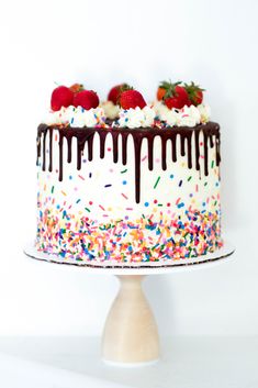 a cake with white frosting, chocolate and sprinkles has strawberries on top