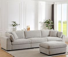 a living room with a large sectional couch and footstool next to a window