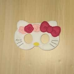 a hello kitty mask with red bows and a bow on the side, sitting on a wooden surface