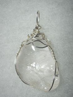 Clear Quartz Pendant Wire Wrapped in .925 Sterling Silver Round Wire This inspiring stone exhibits transparent clarity with multiple internal reflection and refraction with some iridescent display. As it is clear, reflecting and refracting any background color, it is very versatile and can be worn with any color of clothing; a non-standard shape, non-uniform surface, and internal crystal plane/fine fracture reflection and refraction make this stone of more appeal to an artistic view than a puris Unique Clear Healing Crystals, Clear Healing Crystals, Handmade Elegant Silver Crystals, Silver Gemstone Crystals For Jewelry Making, Clear Quartz Gemstone Crystals, Unique Silver Mineral Crystal, Elegant Silver Gemstone Crystals, Elegant Silver Crystals For Gift, Elegant Silver Crystals As A Gift