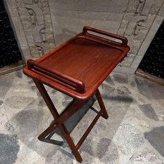 a wooden tray sitting on top of a folding chair in front of a stone wall