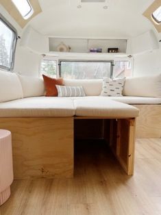 the inside of a camper with white couches and wooden tables in front of windows