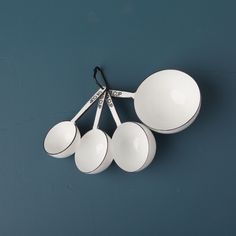 four white measuring spoons are hanging from a hook on a blue wall with black handles