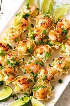 shrimp taco bites on a white plate with limes and cilantro garnish