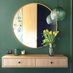 a vase with yellow flowers sitting on top of a wooden dresser next to a round mirror