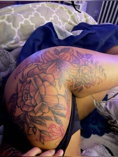 a woman laying on top of a bed next to a flower covered back with tattoos