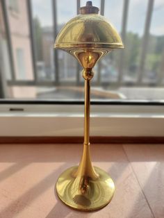 a gold colored table lamp sitting in front of a window