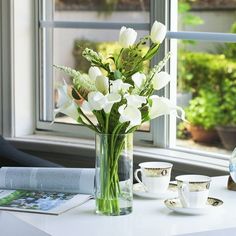 a vase filled with white flowers sitting on top of a table next to a window