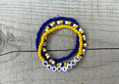 three beaded bracelets with words written in white, yellow and blue beads on a wooden surface