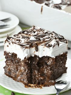 a piece of chocolate cake with white frosting on a green and white plate next to silverware