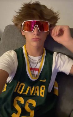 a young man with sunglasses on his head wearing a green and yellow jersey, sitting in a chair