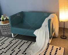 a blue couch with a white blanket on it next to a lamp and potted plant