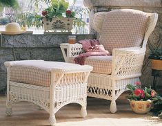 two wicker chairs sitting next to each other in front of a stone wall and potted plants