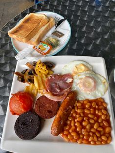 a white plate topped with different types of food on top of a glass table next to a cup of coffee