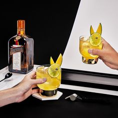 two people holding glasses with drinks in front of them and a bottle on the table