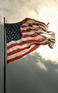 an american flag is flying in the wind on a cloudy day with sun peeking through clouds