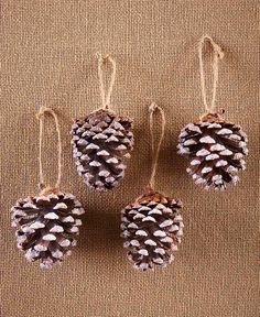 three small pine cones hanging from hooks on a brown fabric background with white thread and twine