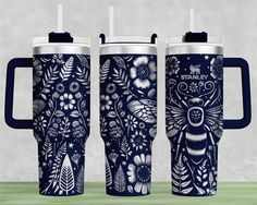 two travel mugs with blue handles and floral designs on them, sitting next to each other