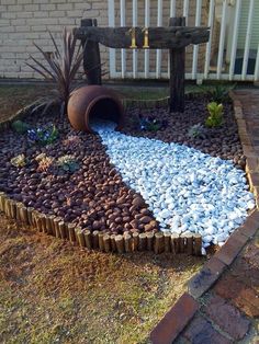 a garden area with rocks and gravel in the shape of a circle, next to a white picket fence