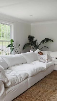 a person laying on a white couch in a living room with palm trees behind them