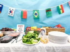 a table topped with plates and bowls filled with food next to a blue wall covered in paper streamers