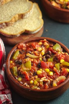 a wooden bowl filled with chili and beans on top of a table next to bread