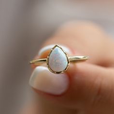 a woman's hand holding a gold ring with a white opal