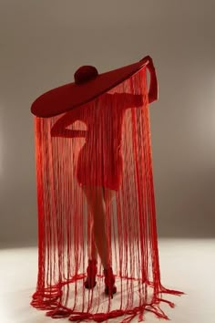 a woman is standing in front of a red object with long strands on the floor